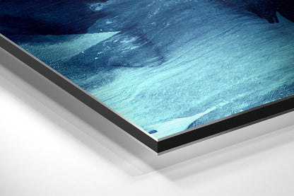 Angled close-up of framed aluminium dibond wall art displaying abstract blue and turquoise wave patterns with black border.