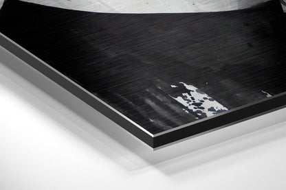 Angled perspective view of brushed aluminum Dibond wall art with white and blue abstract design on black surface.