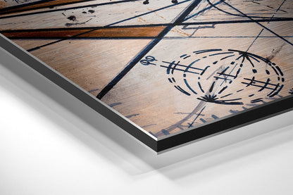 Close-up angled view of brushed aluminum Dibond wall art showing wooden plank texture with blue ink geometric drawings and stitch-mark patterns.