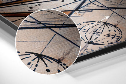 Close-up detail of brushed aluminum wall art showing black geometric line patterns and radiating starburst designs on light wood grain surface.