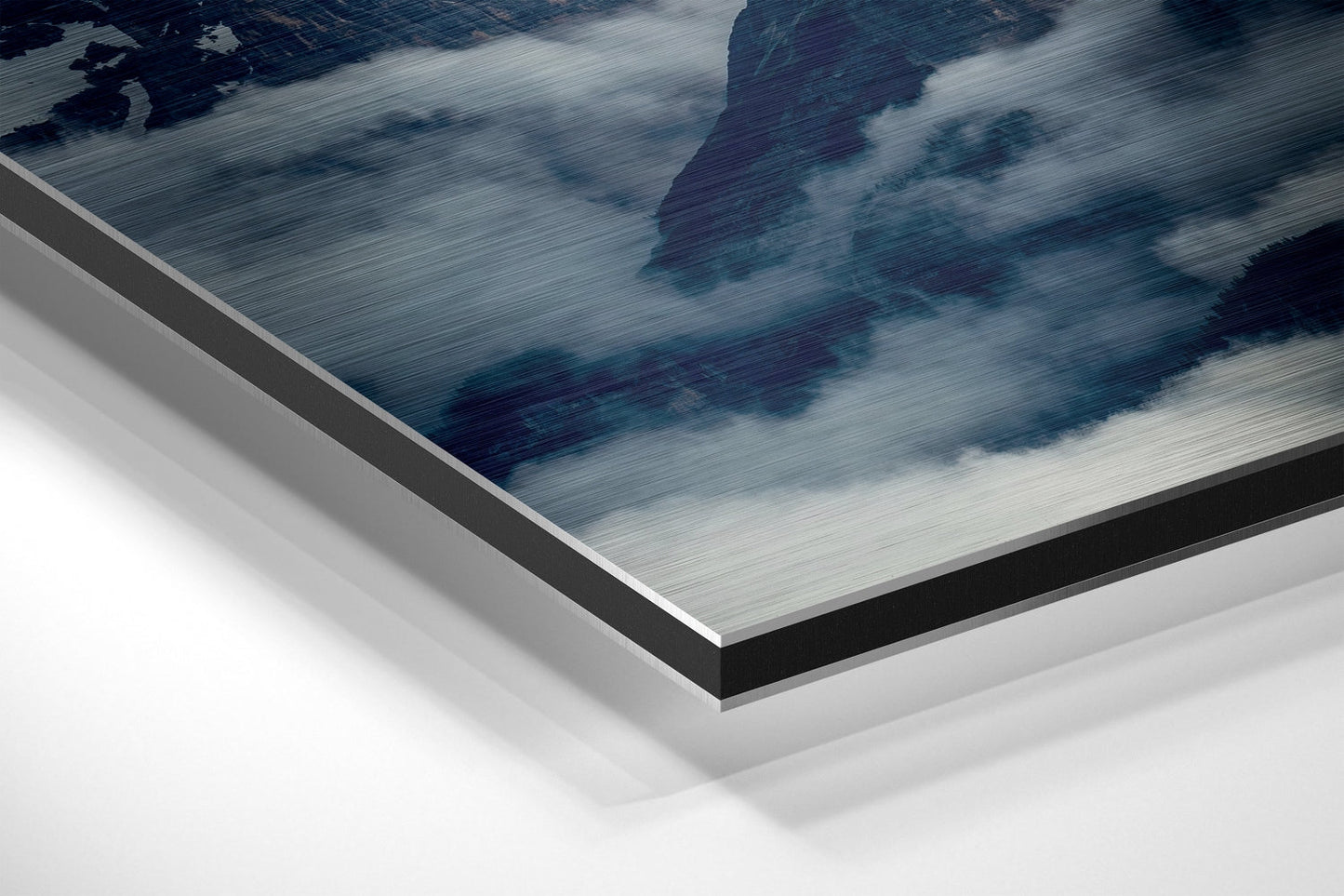 Close-up angled view of brushed aluminium Dibond panel showing layered edge construction with mountain landscape artwork featuring blue tones and white clouds.