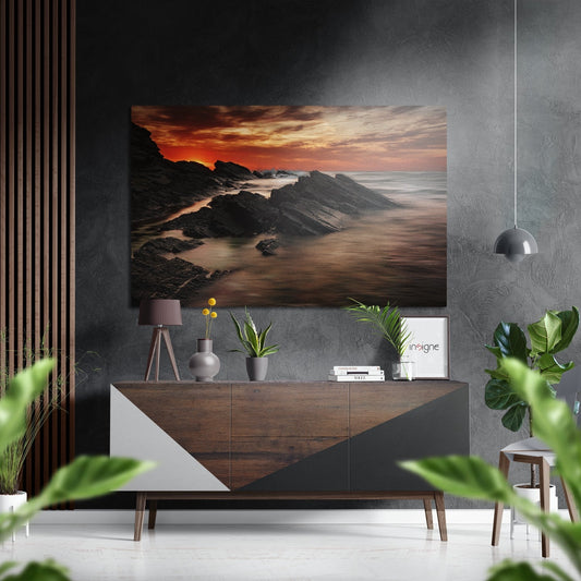 Coastal sunset artwork displayed above a mid-century modern wooden dresser in a minimalist gray interior setting.