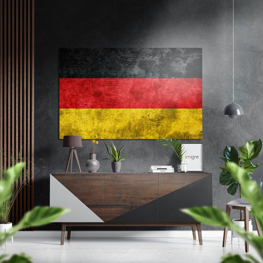 Grunge textured German flag with black, red, and yellow horizontal stripes displayed on gray wall above wooden sideboard in modern interior.