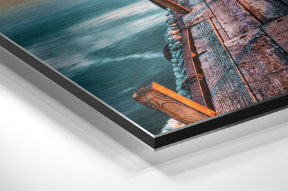Close-up angled view of brushed aluminum Dibond wall art featuring a wooden dock with turquoise water and rope details.