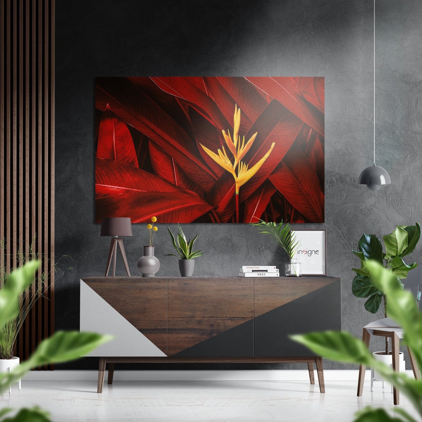 Red and yellow tropical flower metal wall art displayed above a wood and white dresser in a modern gray interior with plants and pendant lamp.