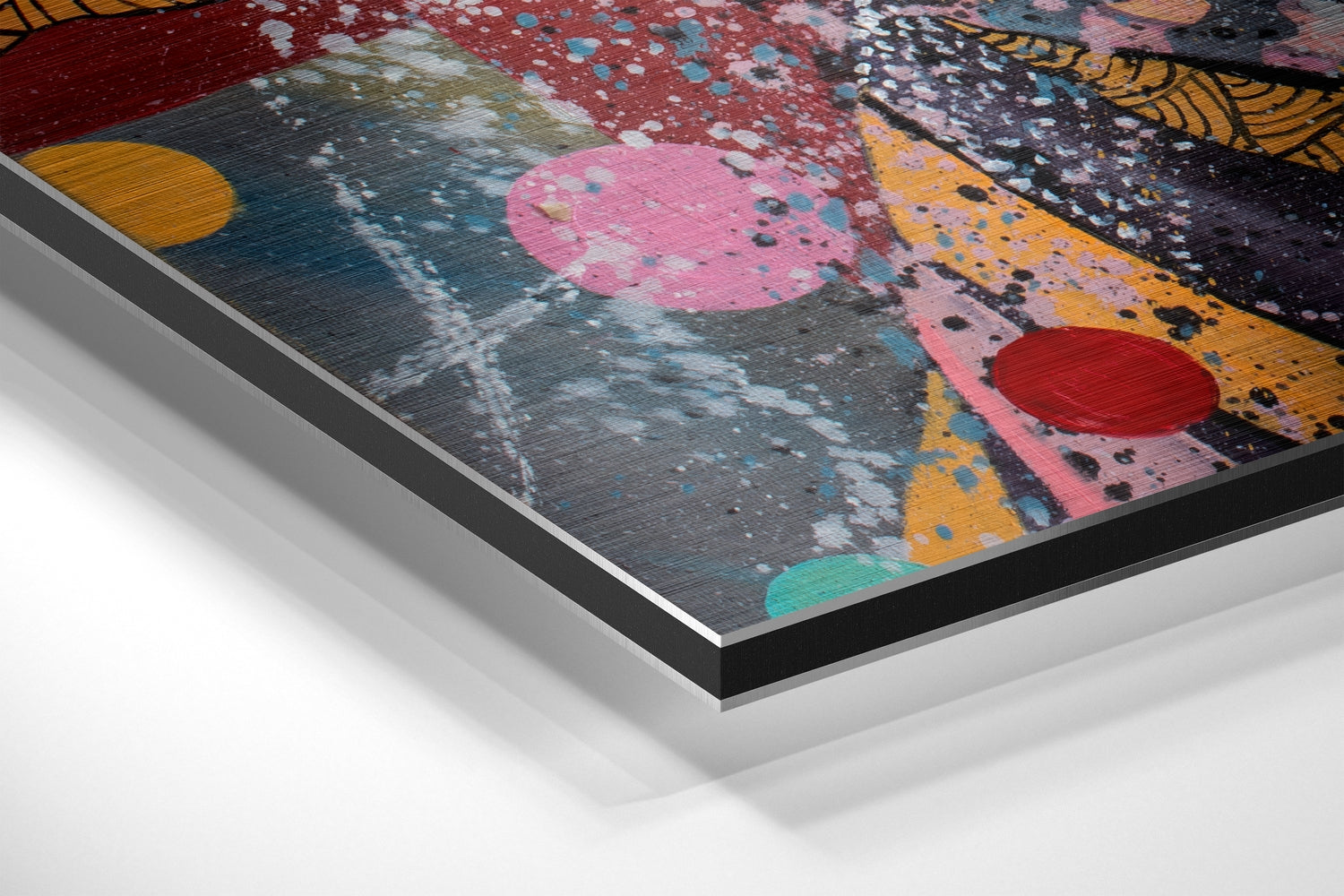 Angled perspective of colorful abstract wall art on brushed aluminum with geometric shapes, splatter effects, and layered mounting edges visible.