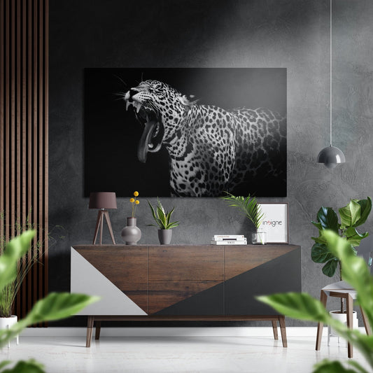 Black and white leopard snarling portrait displayed above wooden console table in modern gray interior with plants and decor.