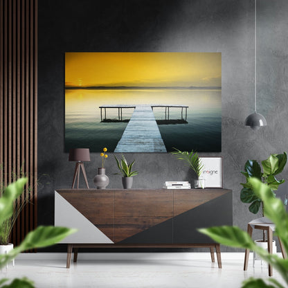Brushed aluminium Dibond wall art displaying a wooden pier extending into calm golden-sunset waters, mounted above a mid-century console in a modern interior setting.