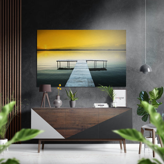 Brushed aluminium Dibond wall art displaying a wooden pier extending into calm golden-sunset waters, mounted above a mid-century console in a modern interior setting.