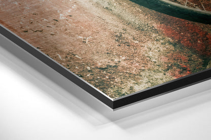 Close-up angled view of layered Dibond wall art showing black and white composite backing beneath weathered rustic surface with brown, green, and red tones.