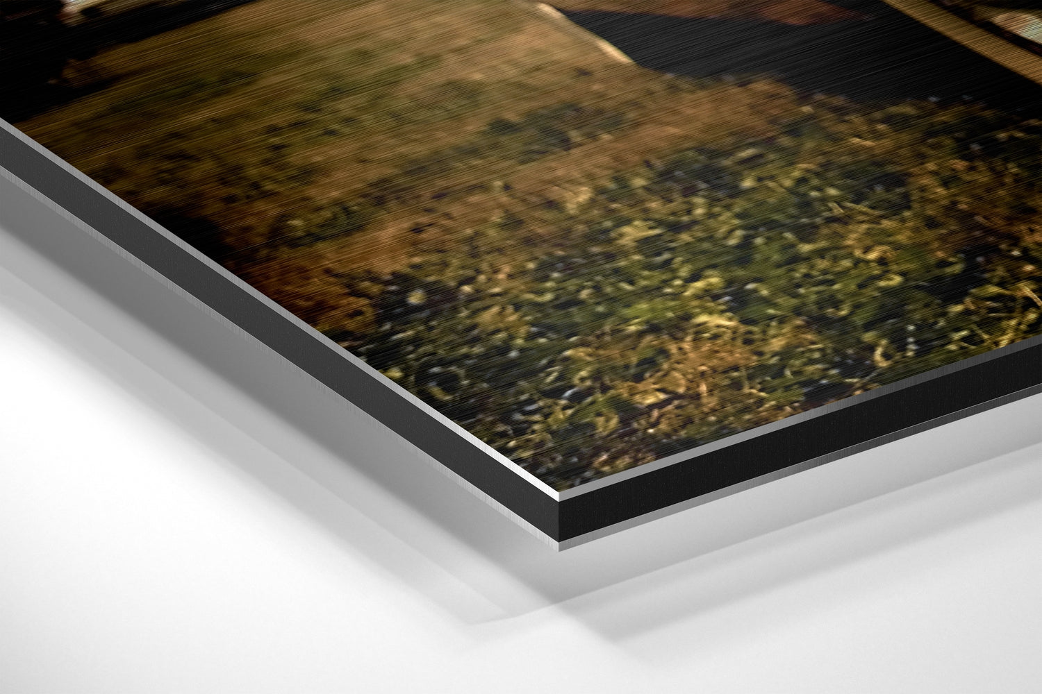Angled close-up view of layered Dibond print showing black frame edge and white backing material against white surface.