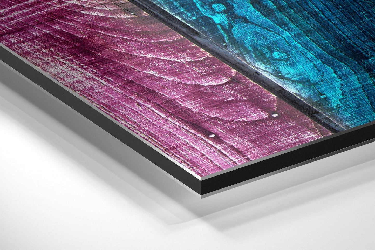 Angled view of brushed aluminum Dibond wall art displaying magenta and cyan geometric patterns with visible layered edge and mounting system.