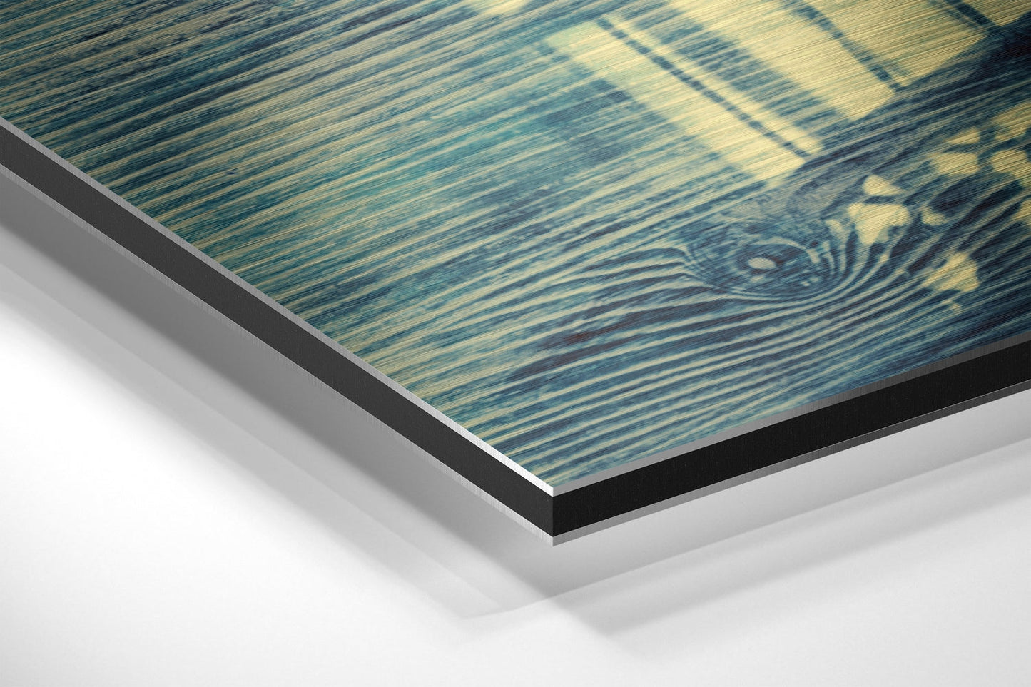 Close-up angled view of layered Dibond wall art showing blue-green brushed aluminum surface with decorative cage pattern and black edge trim.