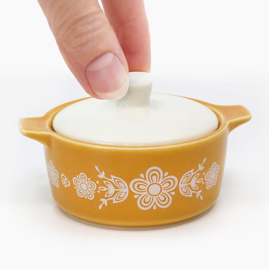 Hand lifting the white lid of the mustard yellow Butterfly Gold mini casserole trinket box
