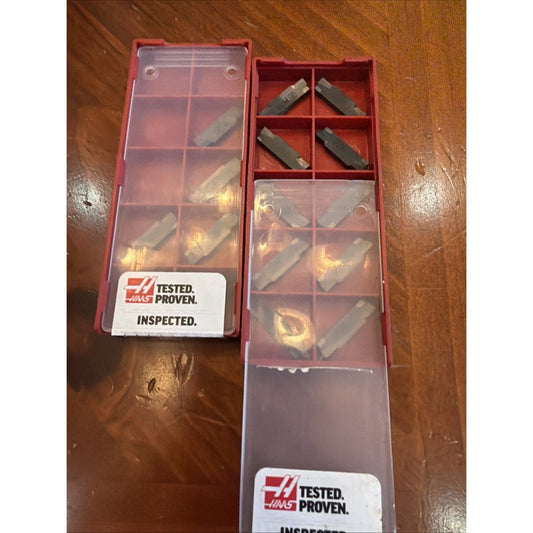 Two red Haas storage boxes with clear lids containing carbide insert cutters on wooden surface, labeled "Tested. Proven. Inspected.