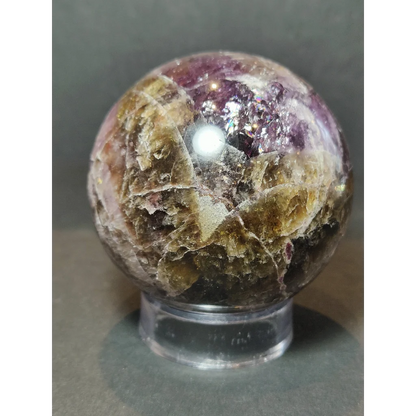 A polished cacoxenite amethyst sphere sculpture with multicolored crystalline texture and green mineral accents
