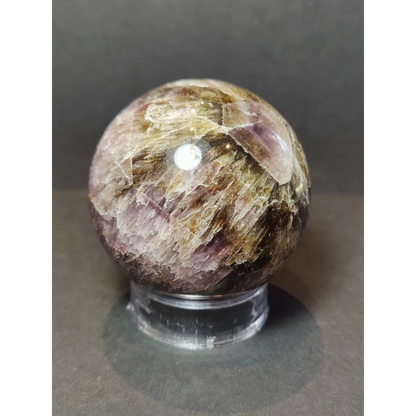 A polished sphere sculpture of cacoxenite amethyst displaying intricate purple and golden geode layers