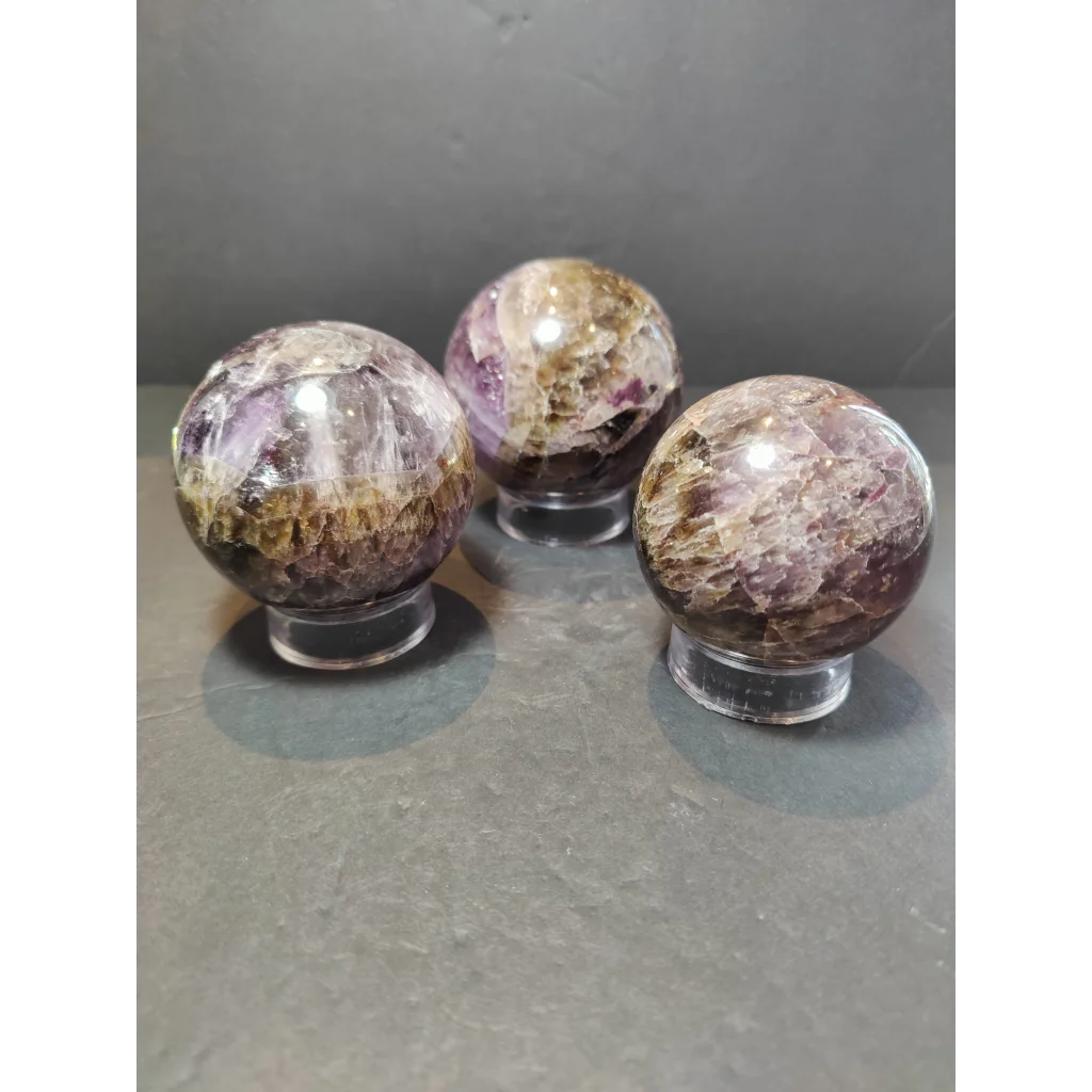 Three polished cacoxenite amethyst sphere sculptures with deep purple and golden-brown swirling patterns