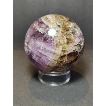 A polished sphere sculpture of cacoxenite amethyst with swirling purple and golden-brown mineral layers