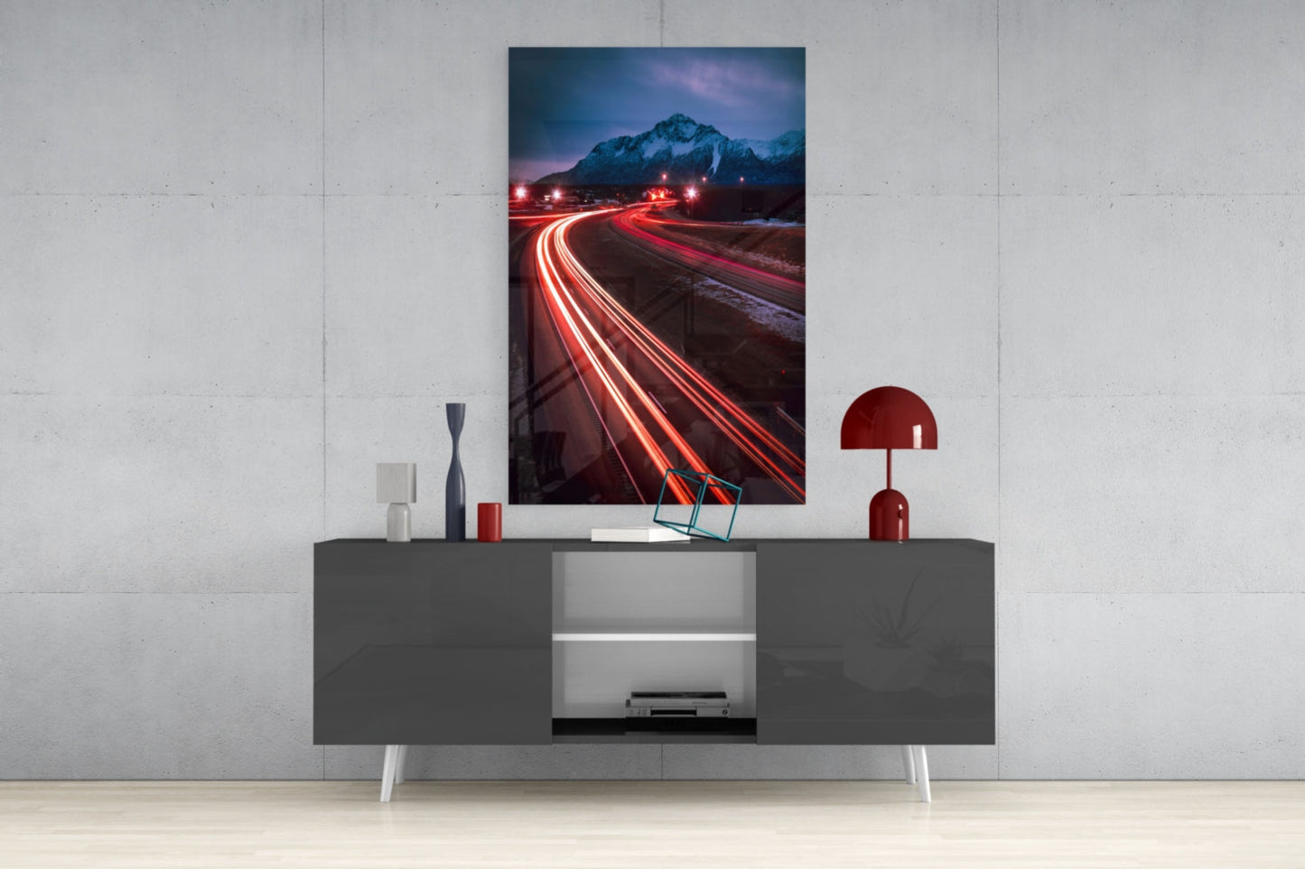 Road Glass Wall Art displayed above a gray media console, showing a long-exposure photograph of red car light trails curving toward a snow-capped mountain at dusk.