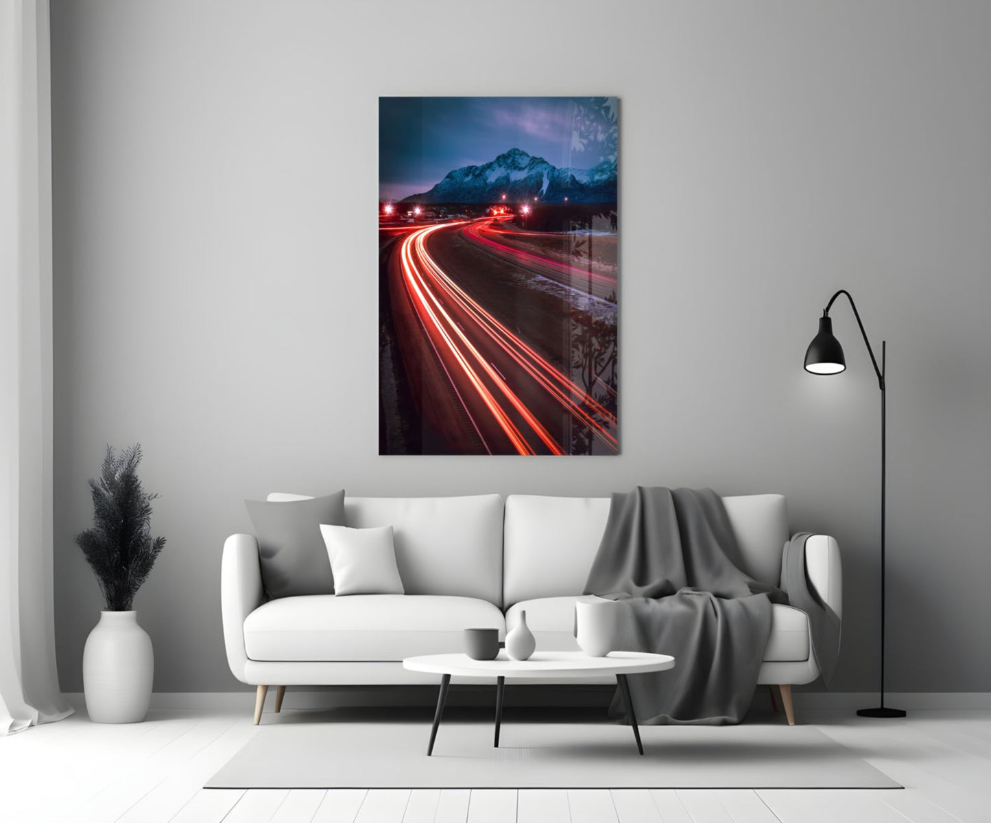 Road Glass Wall Art displayed above white sofa showing red car light trails curving toward snow-capped mountain at twilight.
