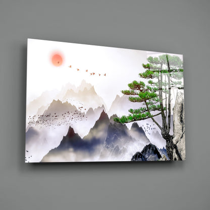 Glass wall art displaying misty mountains, a red sun, flying birds, and a gnarled tree with green foliage against gray wall.