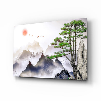 Glass wall art displaying misty mountains, a gnarled pine tree on rocky outcrop, red sun, and flying birds in muted tones.