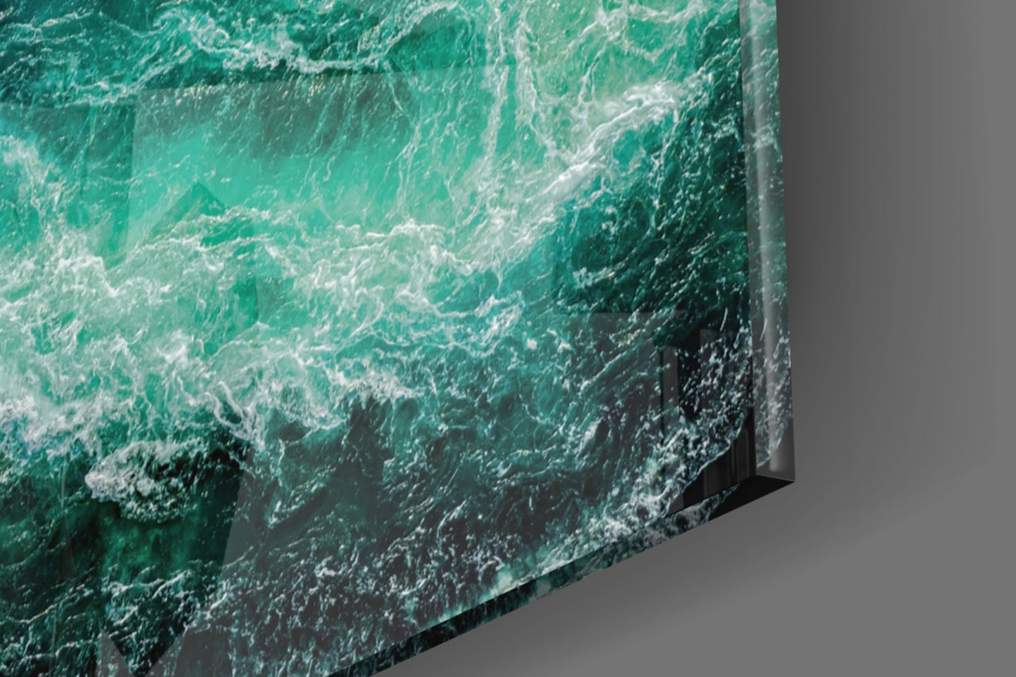 Angled view of glass wall art displaying turquoise ocean waves with white foam against gray background.
