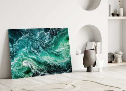 Green Waves Glass Wall Art leaning against white wall in minimalist interior with sand, shelving, and decorative objects.