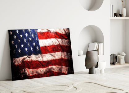 Textured American flag glass art leaning against white wall in minimalist room setting with decorative objects.