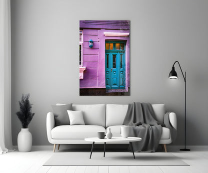 Purple House Glass Wall Art displayed above white sofa showing vibrant pink building facade with turquoise door.