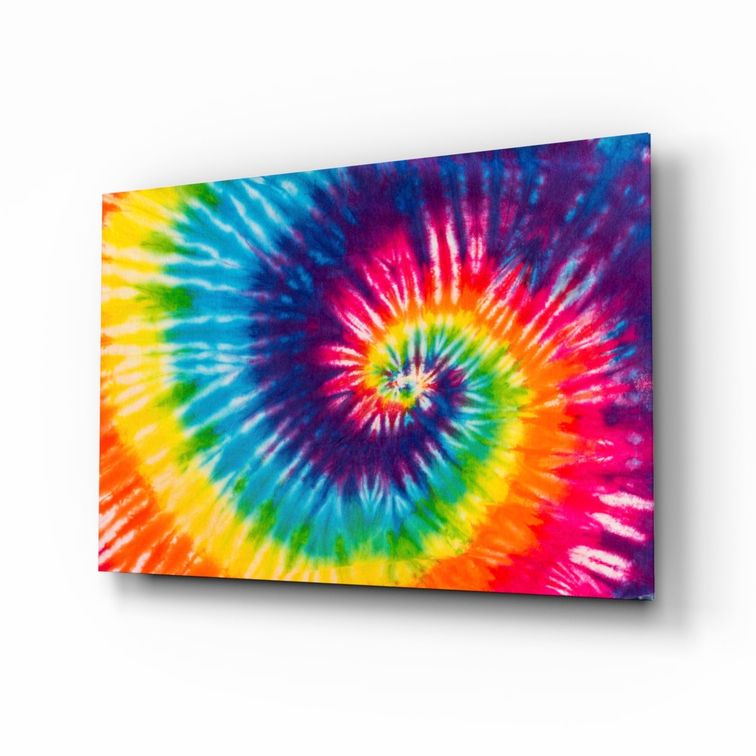Angled perspective view of a vibrant tie-dye pattern glass wall art panel with spiraling rainbow colors radiating from center.
