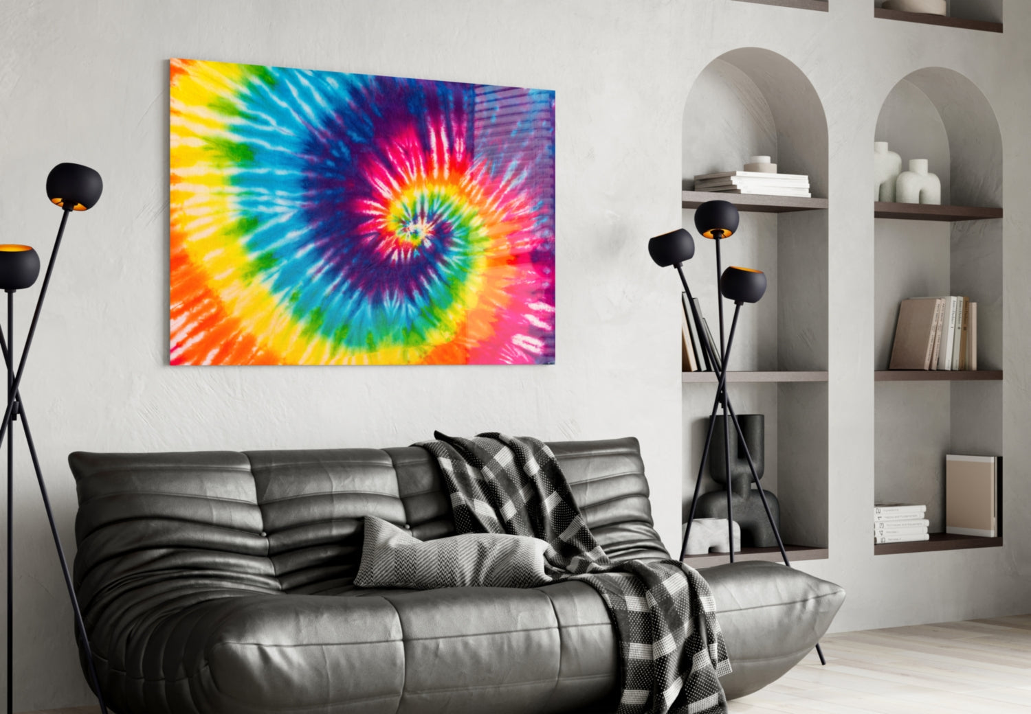 Vibrant tie-dye rainbow spiral glass wall art displayed above black leather sofa in modern living room with shelving.