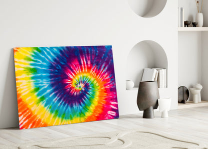 Vibrant tie-dye rainbow spiral glass art leaning against white wall in minimalist room setting with decorative objects.