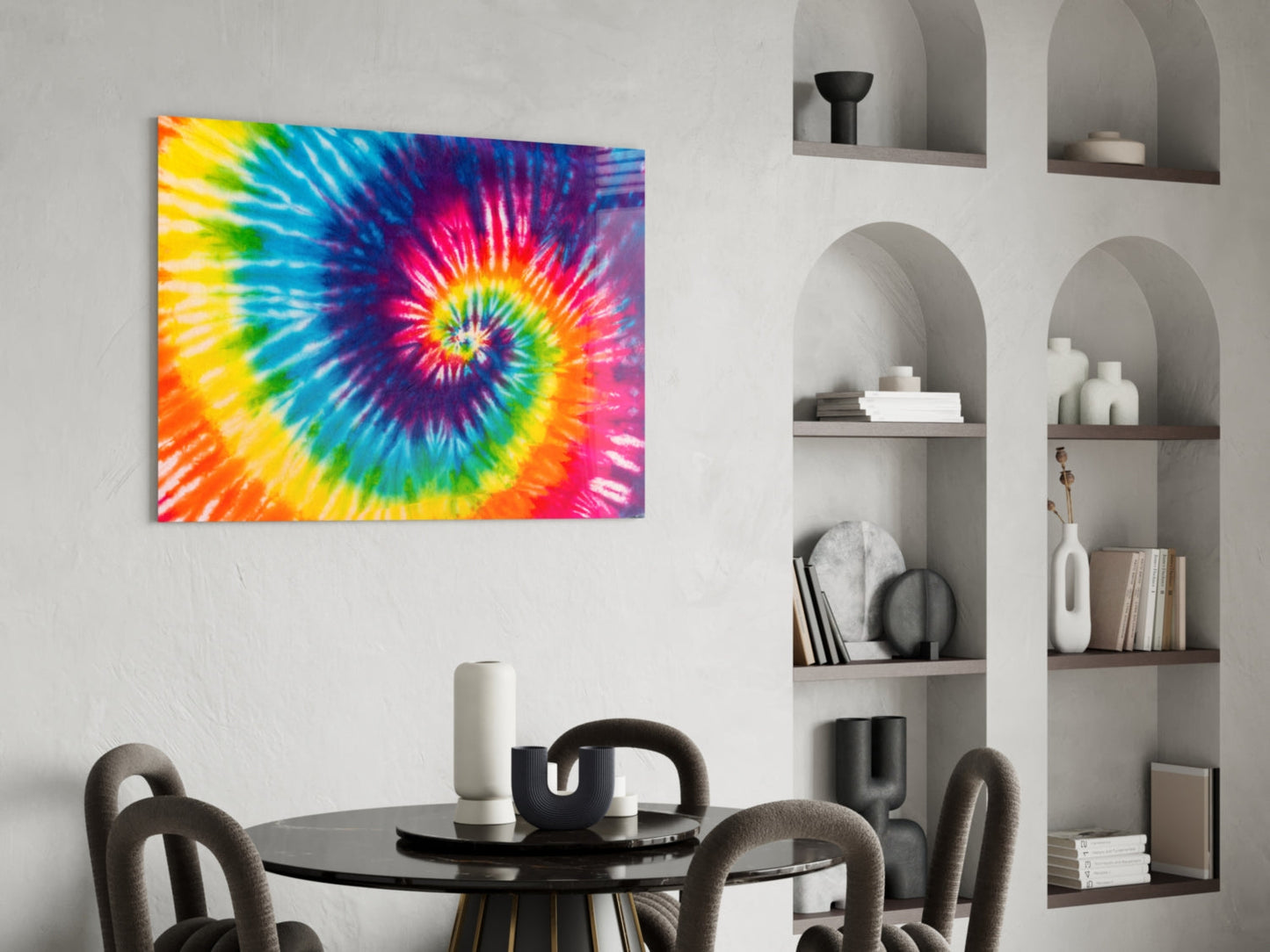 Vibrant tie-dye spiral glass art hanging above black round dining table with gray chairs and white shelving unit.
