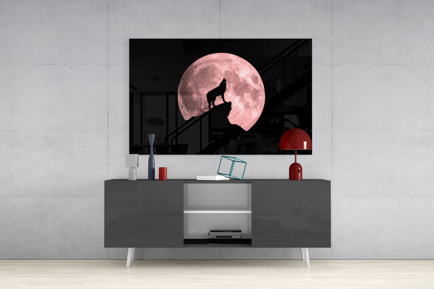 Glass wall art depicting a silhouetted wolf howling on a rocky outcrop against a large pink full moon, displayed on a gray media console.