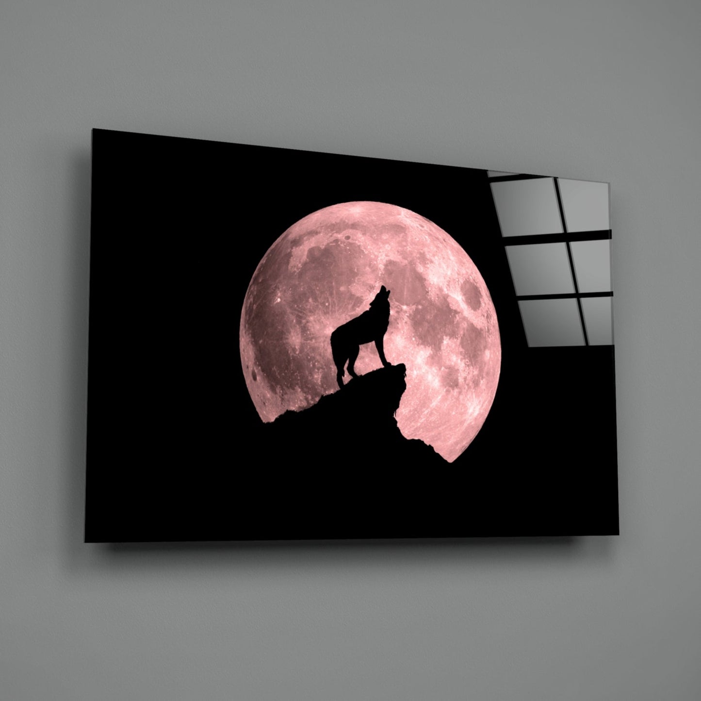 Glass wall art displaying a wolf silhouette howling atop a rocky peak against a large pink full moon on black background.