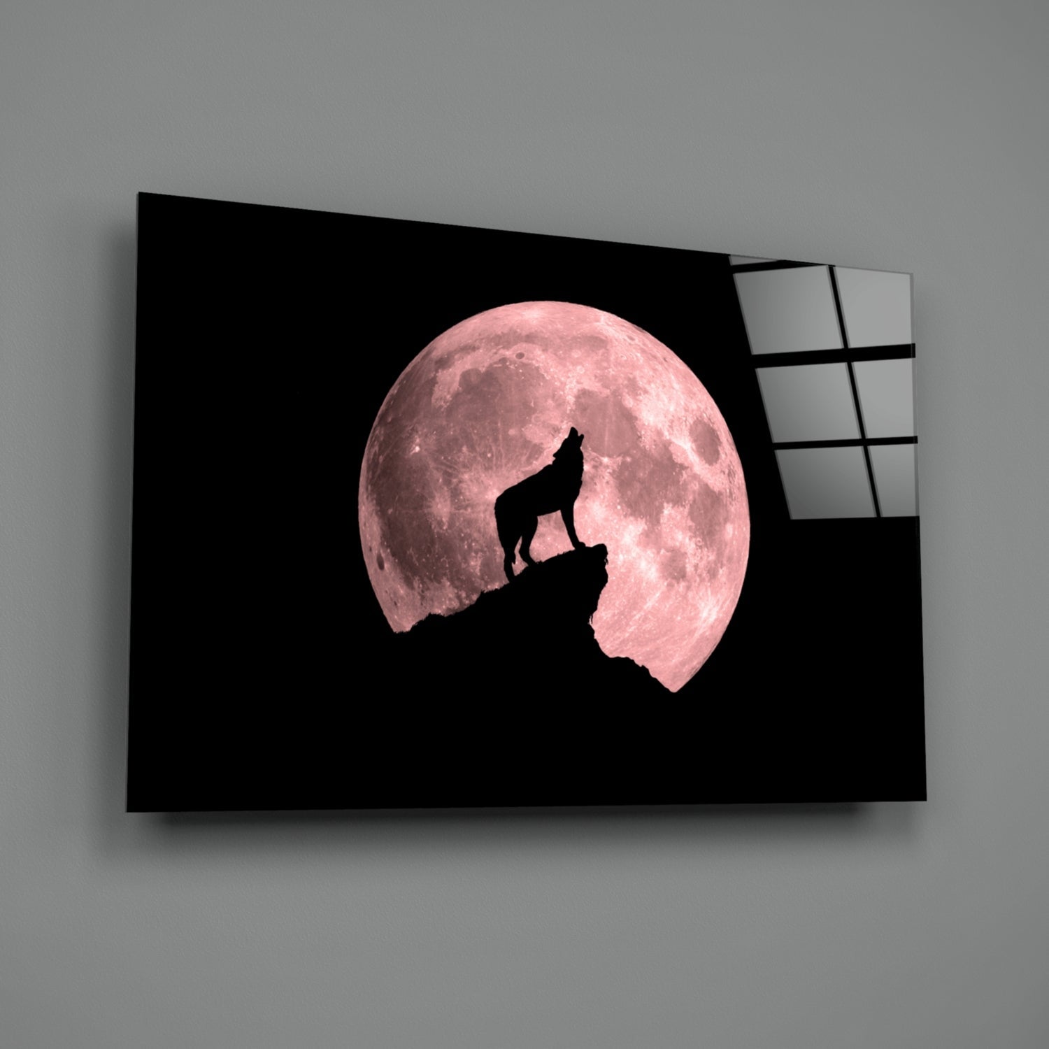 Glass wall art displaying a wolf silhouette howling atop a rocky peak against a large pink full moon on black background.