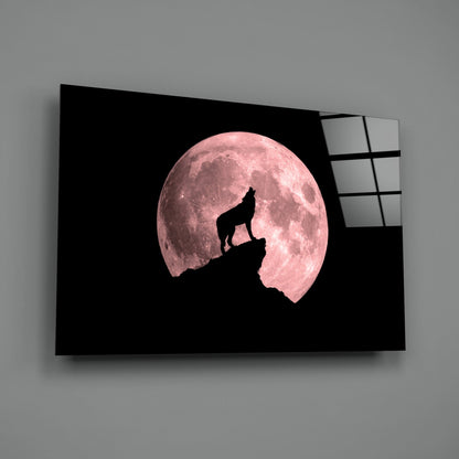 Glass wall art displaying a wolf silhouette howling atop a rocky peak against a large pink full moon on black background.