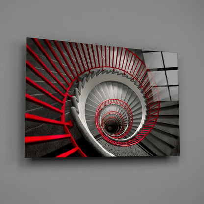 Aerial view of a spiral staircase with red metal railings descending into darkness, captured from above.
