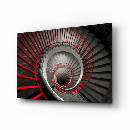 Aerial view of a spiral staircase with red railings descending into darkness, rendered in grayscale with red accents.