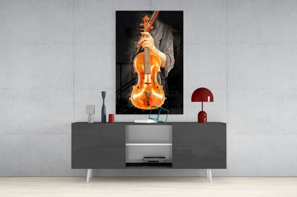 Violin glass wall art depicting a glowing amber violin with bow displayed above a gray media console in a modern interior setting.
