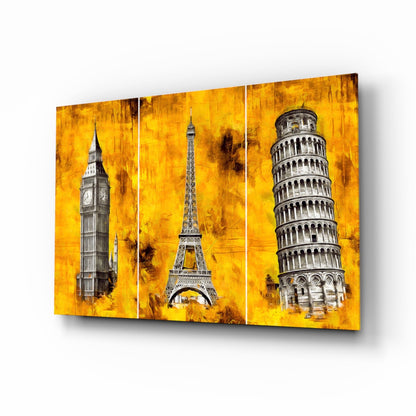 Three-panel glass wall art featuring Big Ben, Eiffel Tower, and Leaning Tower of Pisa against a textured golden yellow background, displayed at an angle.