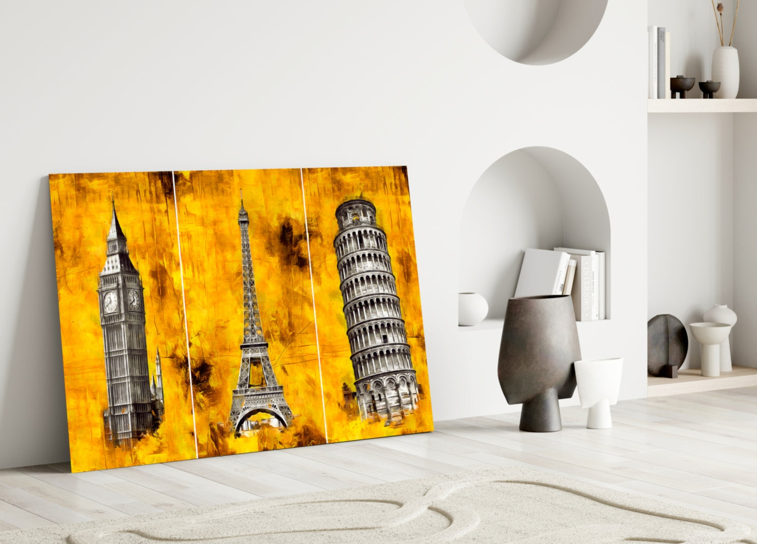Three Towers Glass Wall Art leaning against white wall in minimalist room, showing yellow background with Big Ben, Eiffel Tower, and Leaning Tower of Pisa.