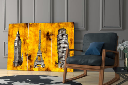 Three-panel glass wall art featuring Big Ben, Eiffel Tower, and Leaning Tower of Pisa on golden yellow textured background, displayed in modern living room setting.
