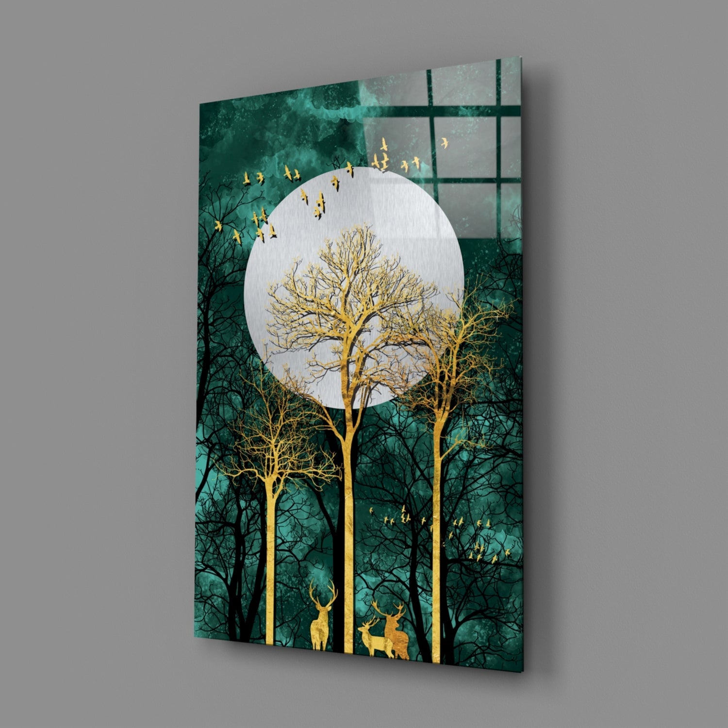 Angled view of glass wall art showing golden trees and deer beneath a white moon against a teal-green forest background.