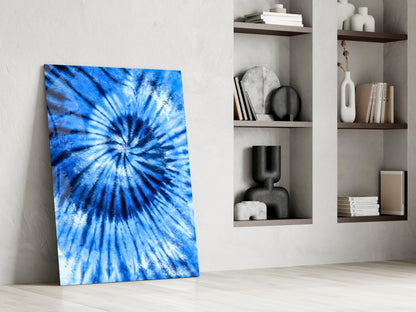 Blue tie-dye mosaic glass panel leaning against white wall beside shelving with decorative objects.