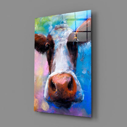 Colorful glass wall art featuring a cow's face with brown and white markings against a vibrant multicolored abstract background, displayed at an angle.