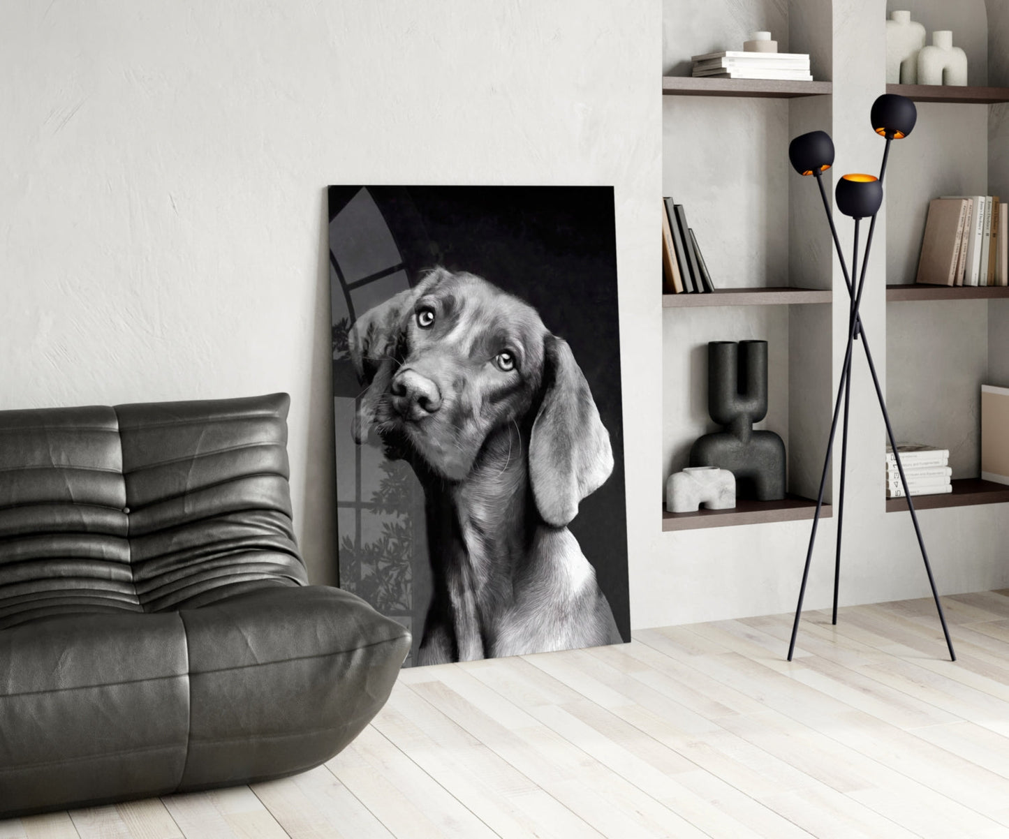 Black and white glass wall art of a dog with tilted head displayed in modern living room with leather sofa and shelving.