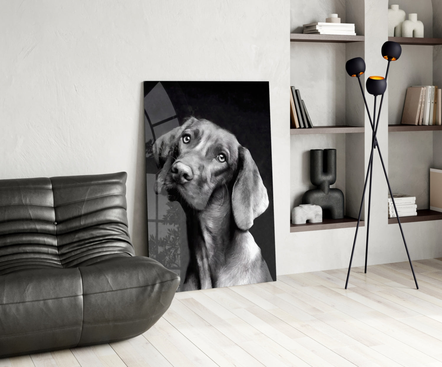 Black and white glass wall art of a dog with tilted head displayed in modern living room with leather sofa and shelving.